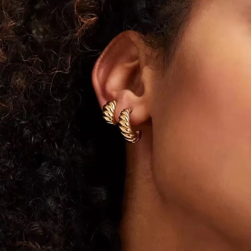 Gold hoop croissant earring worn by a woman with dark curly hair.