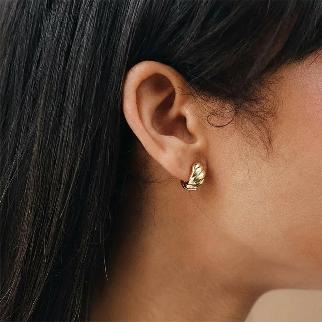 Close-up of an ear wearing a gold croissant hoop earring with dark straight hair.