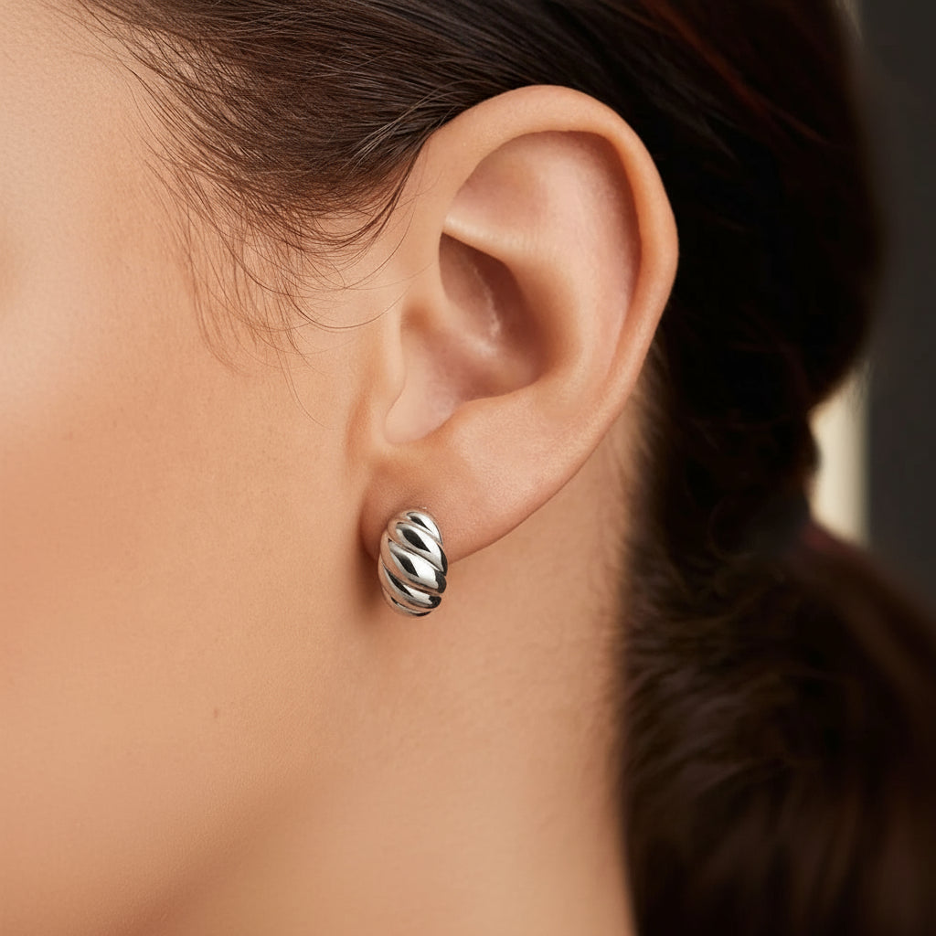 Close-up of an ear wearing a silver croissant earring with a blurred background