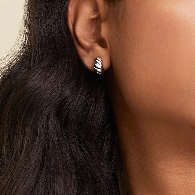 Close-up of an ear wearing a silver hoop earring with a croissant design.